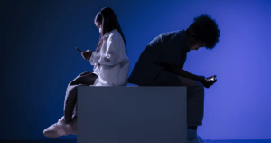 two young people sitting on a box, looking at phones