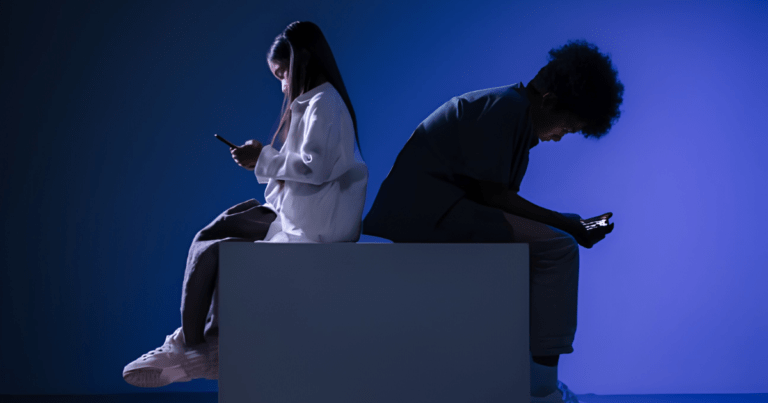 two young people sitting on a box, looking at phones