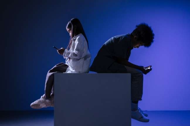 two young people sitting on a box, looking at phones